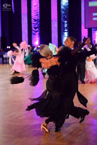 Dancesport competitor: Foreground female dancer: black ballroom dress with large black feather-like fri