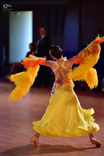Dancesport competitor: Female dancer: yellow Latin dress with large, voluminous yellow and orange feath