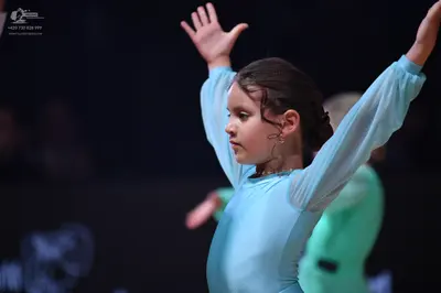 Dancesport competitor: Female dancer in foreground: light blue long-sleeved dance dress with sheer slee