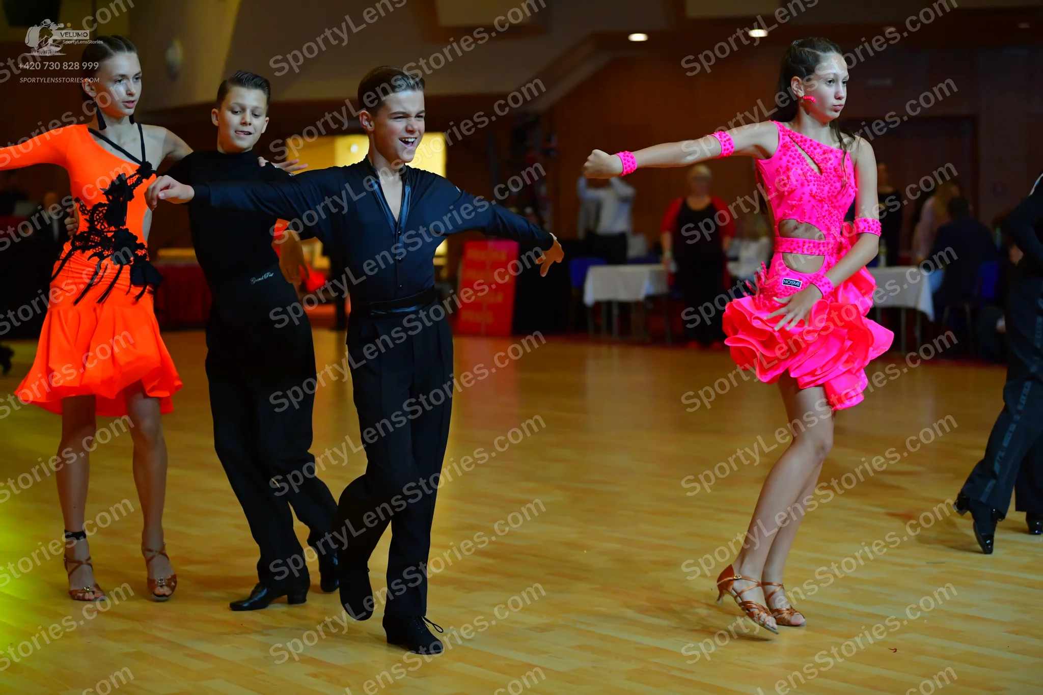 Dancesport competitor: Female dancer 1: bright orange Latin dance dress with black floral applique