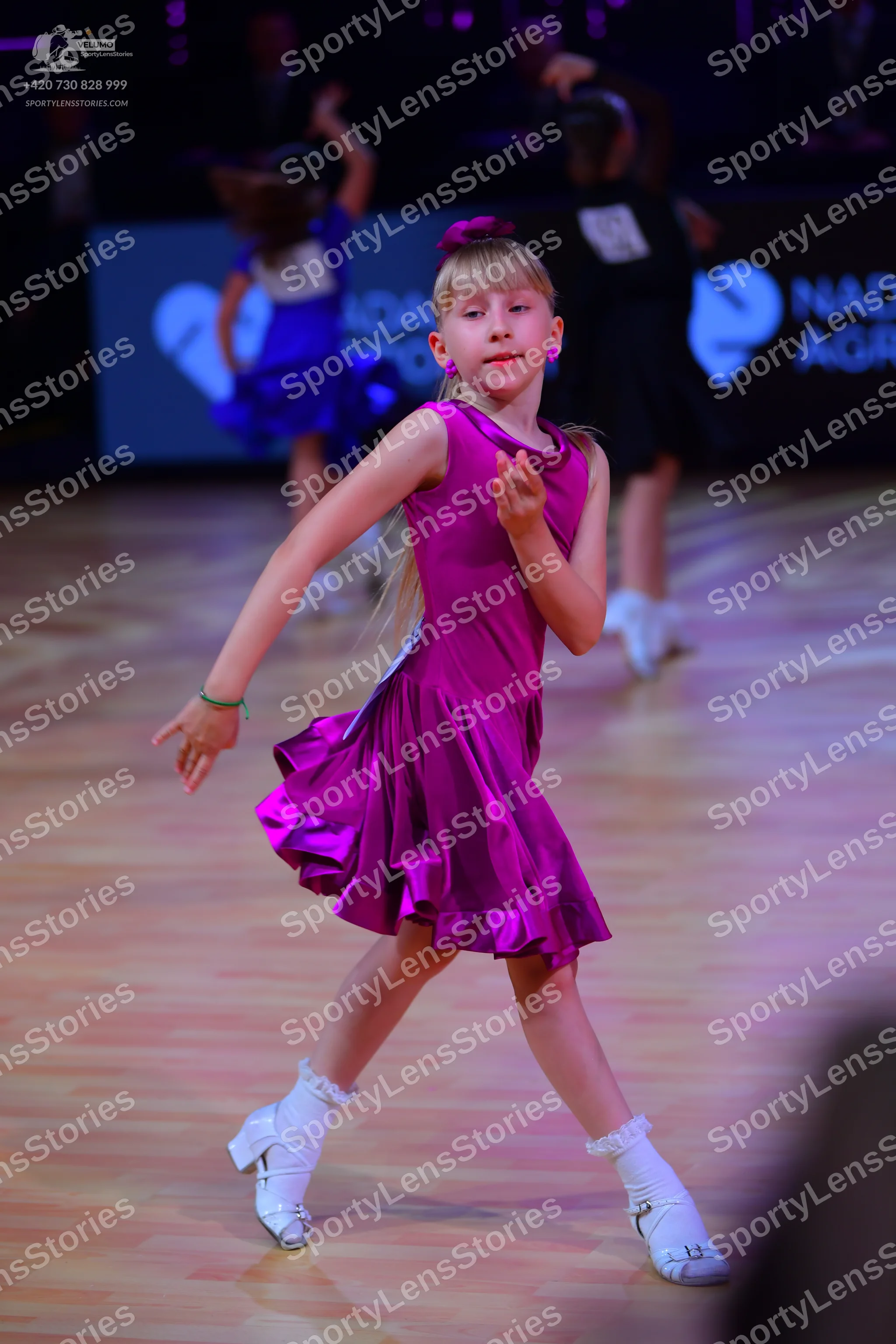 Dancesport competitor: Foreground dancer: magenta satin sleeveless Latin dress with a ruffled skirt, wh