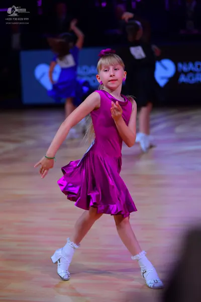 Dancesport competitor: Foreground dancer: magenta satin sleeveless Latin dress with a ruffled skirt, wh