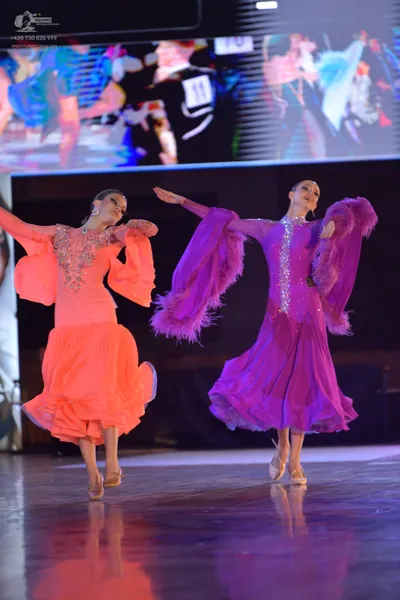 Dancesport competitor #11: Female dancer (left): coral long-sleeved dress with a sequined bodice and large,