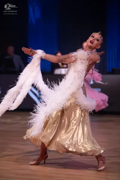Dancesport competitor: Female dancer: gold satin ballgown with a crystal-embellished bodice and sleeves