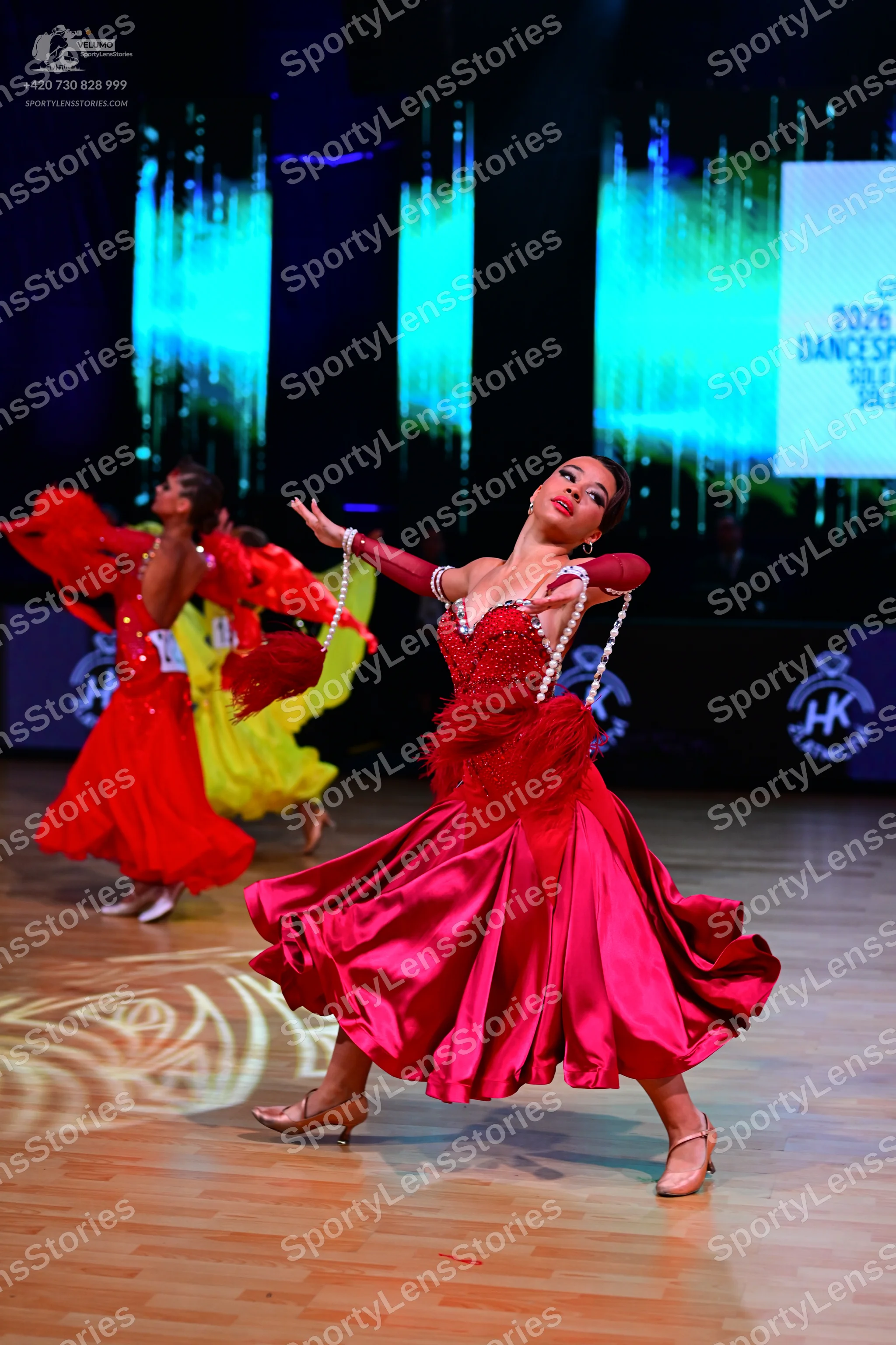 Dancesport competitor: Female dancer in background: red ballroom dress with a large skirt