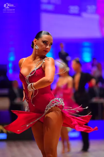 Dancesport competitor: Foreground female dancer: red Latin dress with silver/white sequin swirl pattern