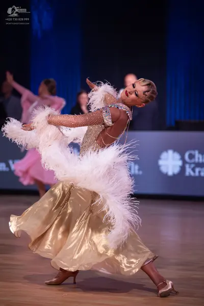 Dancesport competitor: Female dancer in foreground: gold ballgown with a sequined bodice and large whit