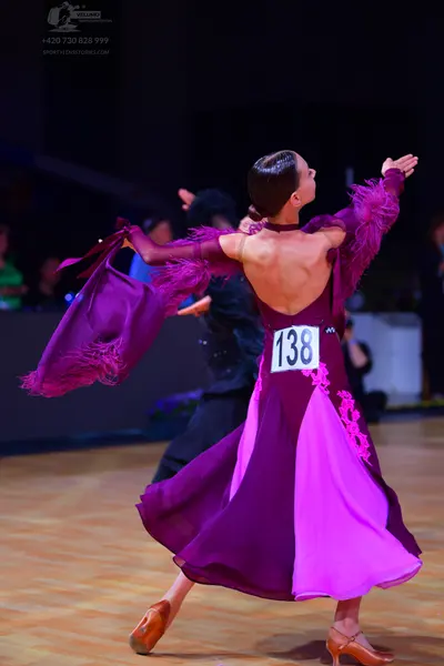 Dancesport competitor: Female dancer: purple long dress with a low back, large flowing sleeves with tex