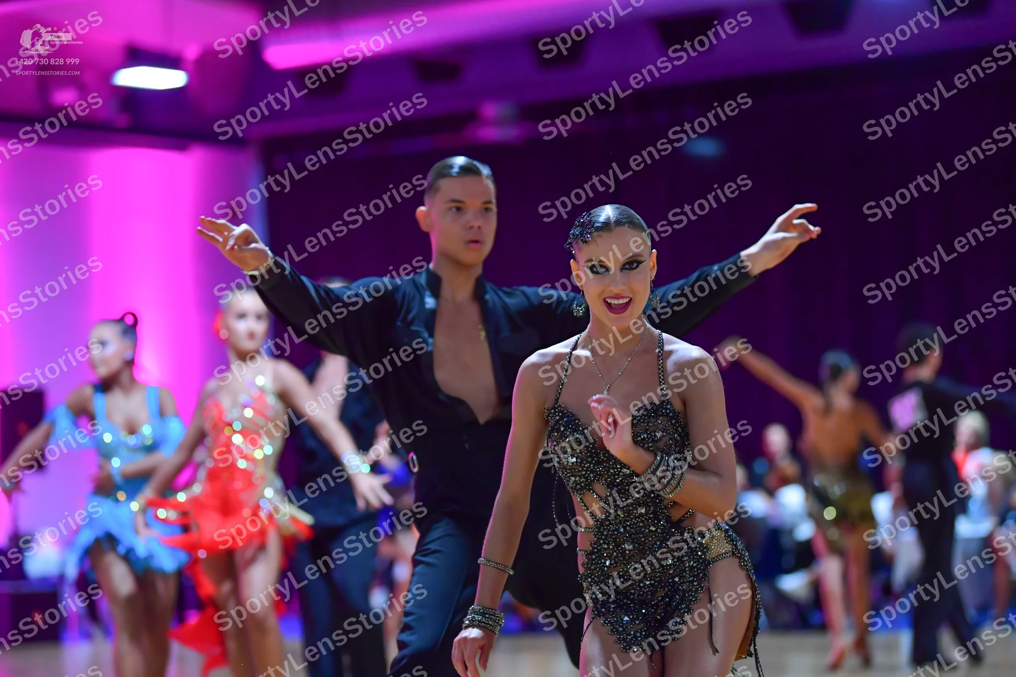 Dancesport competitor: Foreground female dancer: dark, heavily sequined latin dress with thin straps