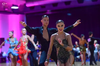 Dancesport competitor: Foreground female dancer: dark, heavily sequined latin dress with thin straps