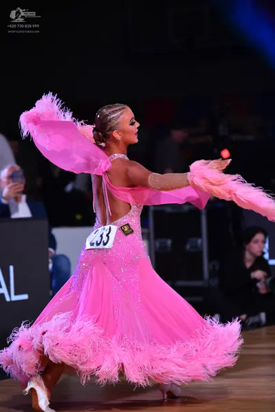 Dancesport competitor: Female dancer: bright pink ballgown adorned with sequins and featuring large pin