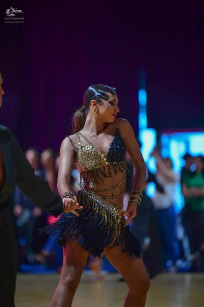 Dancesport competitor: Female dancer: black Latin dance costume with gold/silver sequined bra top and s