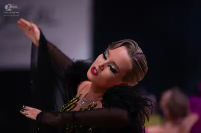 Dancesport competitor: Female dancer in foreground: black Latin-style dress with sheer long sleeves, bl