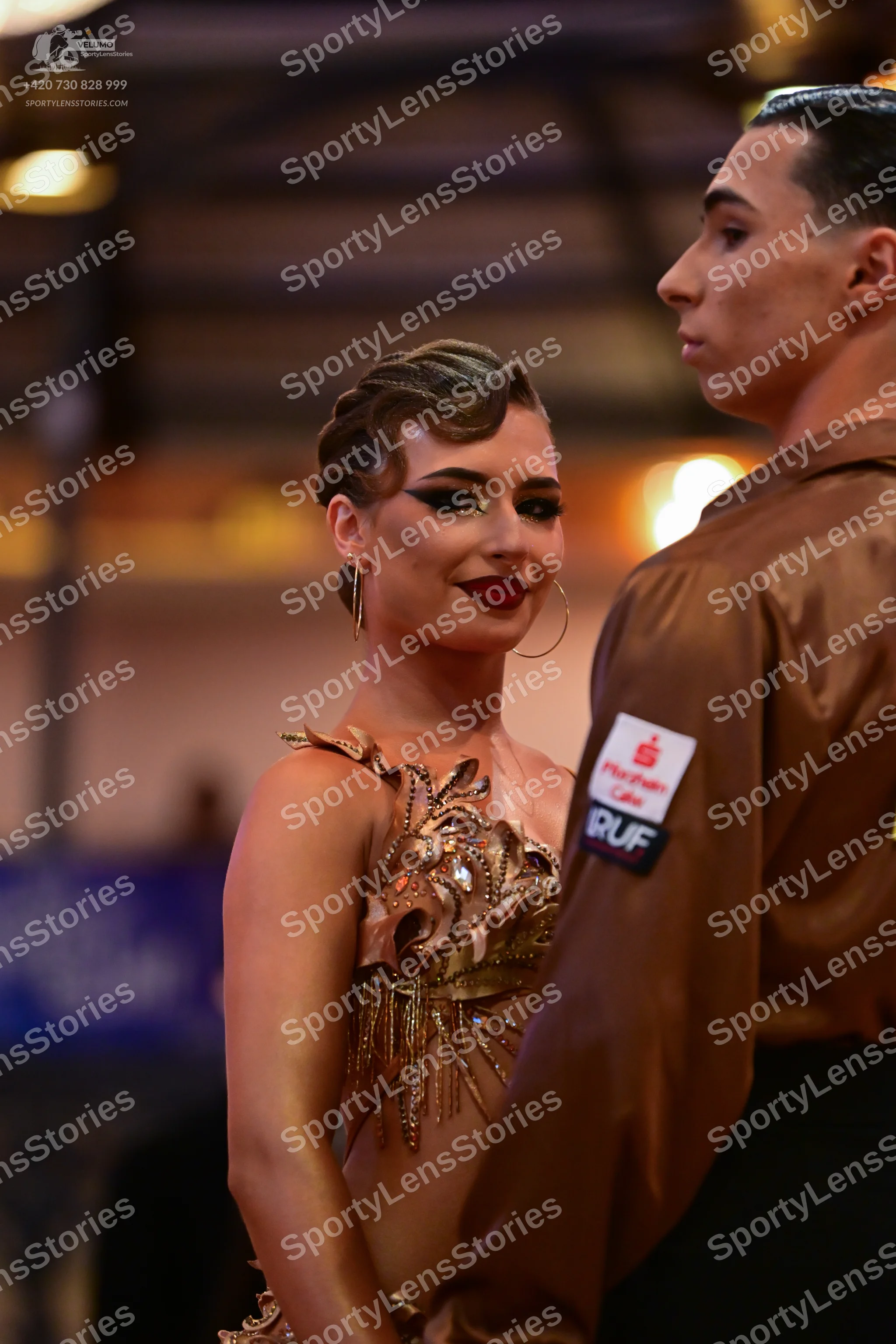 Dancesport competitor: Female dancer: bronze/gold Latin dress featuring metallic/sequin floral patterns