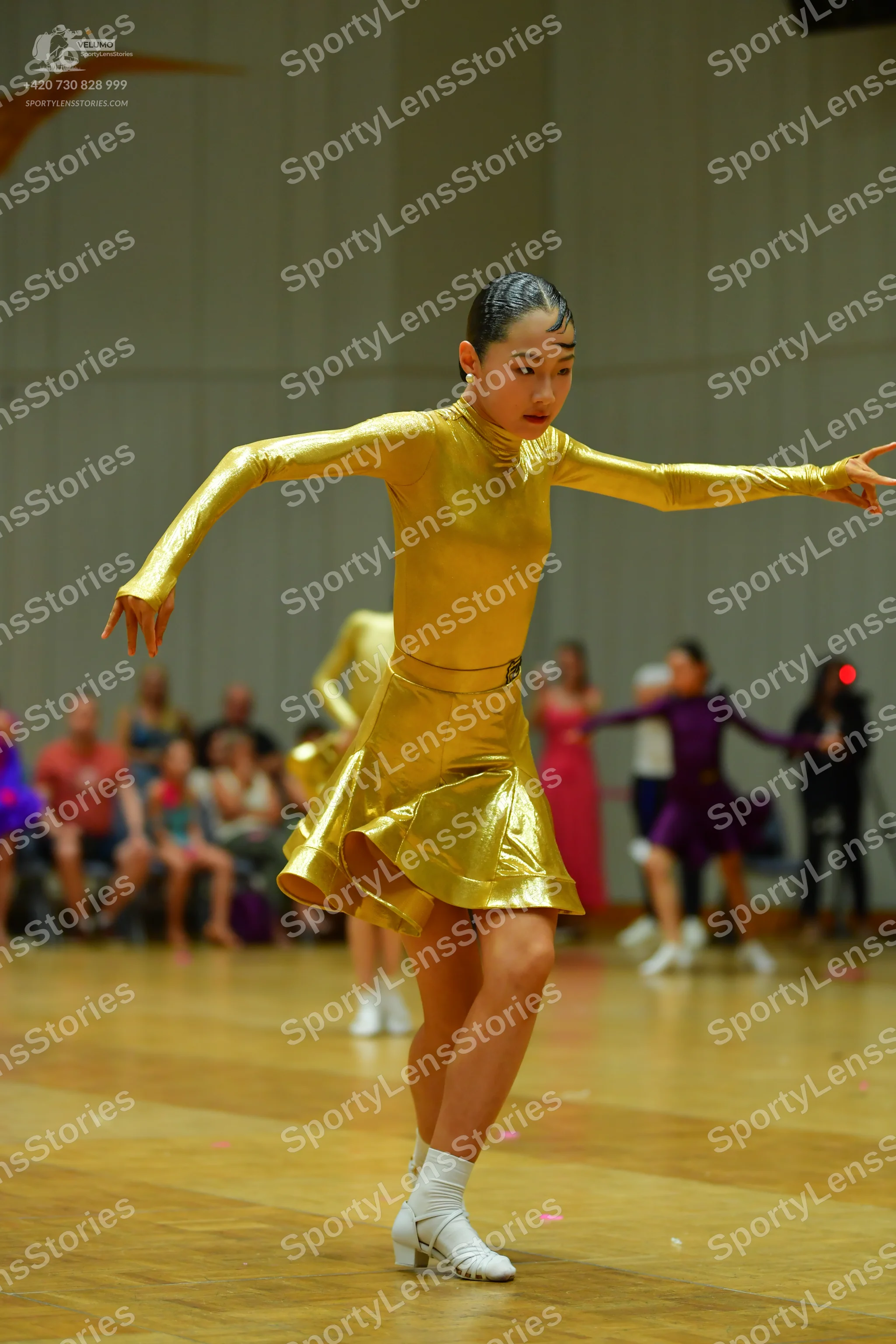 Dancesport competitor: Female dancer in foreground: gold metallic long-sleeved latin dress with a flare