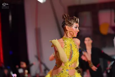 Dancesport competitor: Female dancer: yellow/gold Latin dance dress with sequins, fringe, and cutouts, 