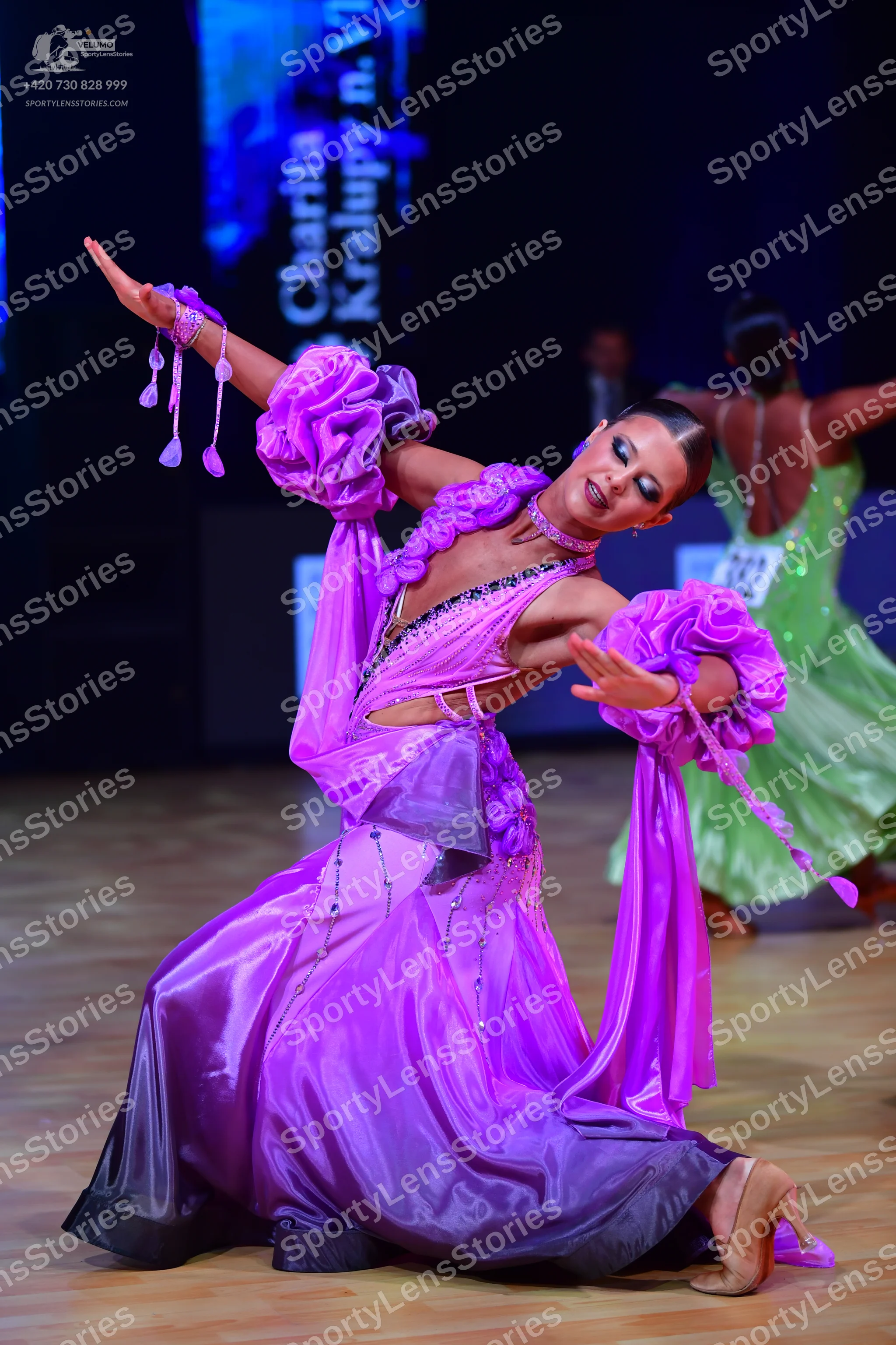 Dancesport competitor: Female dancer (foreground): purple satin-like latin dress with large, voluminous
