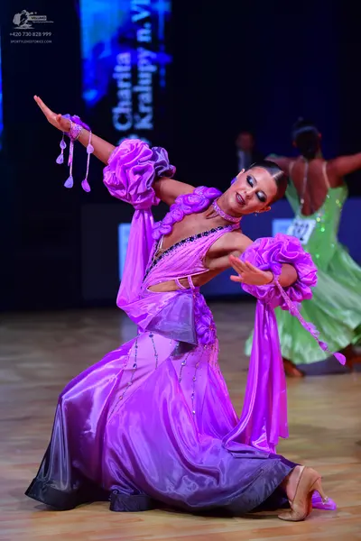 Dancesport competitor: Female dancer (foreground): purple satin-like latin dress with large, voluminous