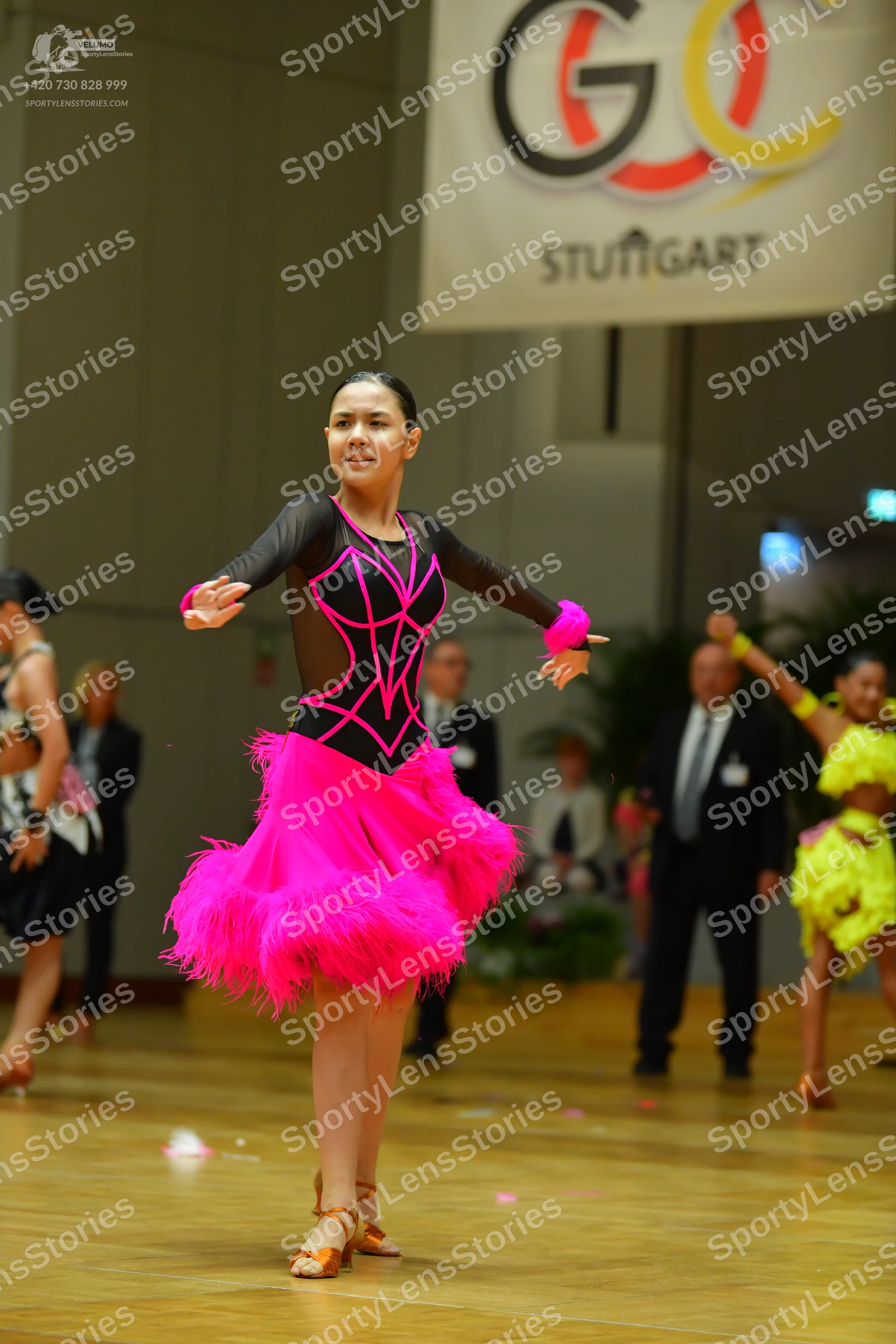 Dancesport competitor: Female dancer in center: black long-sleeved top with magenta accents and a magen