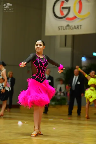 Dancesport competitor: Female dancer in center: black long-sleeved top with magenta accents and a magen