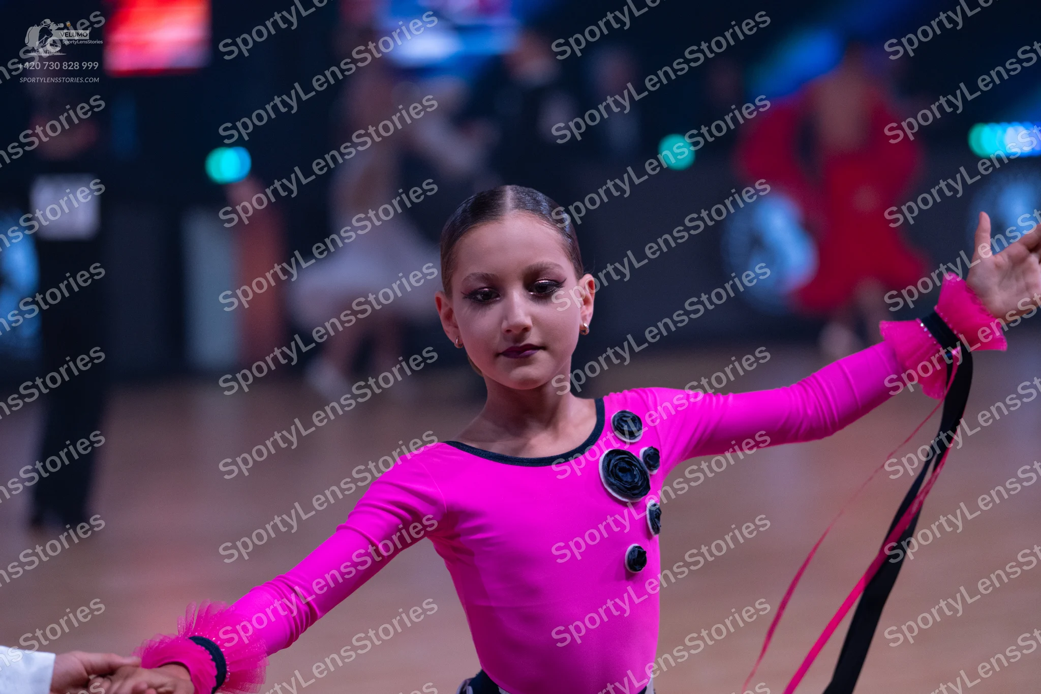 Dancesport competitor: Female dancer: bright pink long-sleeved Latin dress with black circular embellis