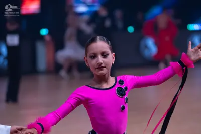 Dancesport competitor: Female dancer: bright pink long-sleeved Latin dress with black circular embellis