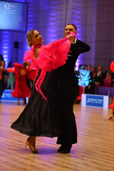 Dancesport competitor: Female dancer: bright pink ruffled top and a long, voluminous black skirt