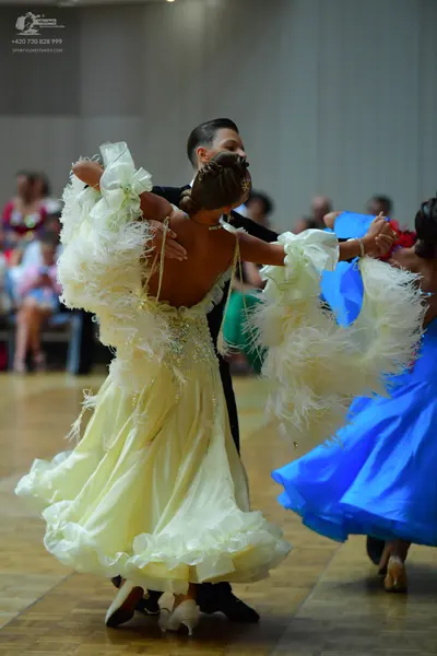 Dancesport competitor: Female dancer: cream-colored ballroom gown with voluminous, ruffled, and feather