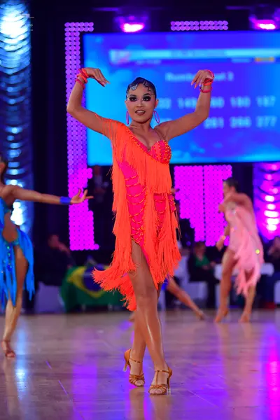 Dancesport competitor: Central female dancer: bright orange latin dress with long fringe and possible s