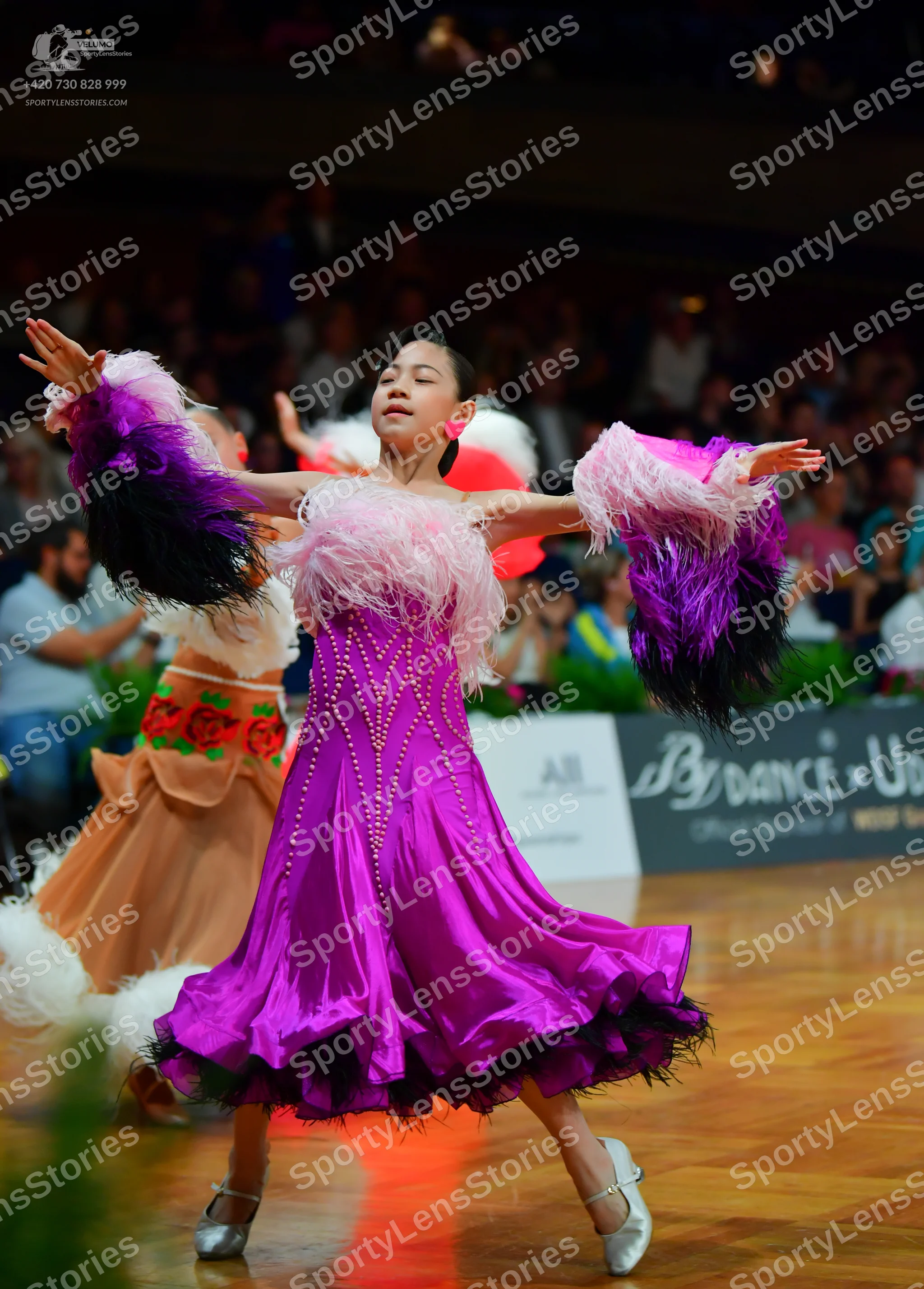 Dancesport competitor: Female dancer in foreground: purple Latin dress with rhinestone embellishments a