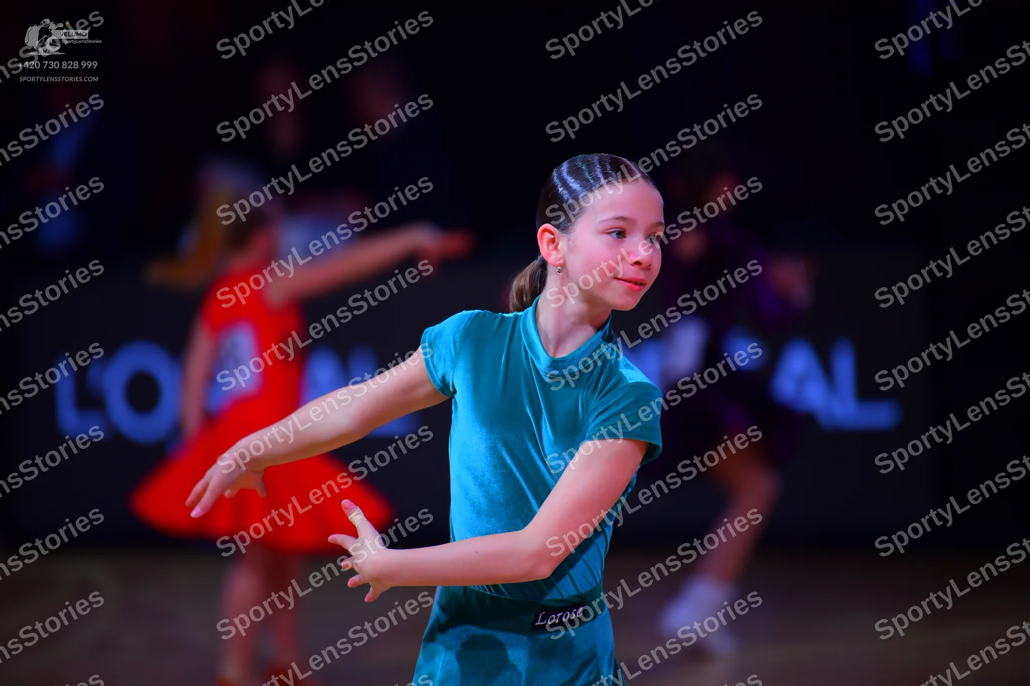 Dancesport competitor: Female dancer in foreground: teal short-sleeved Latin dress in a smooth, shiny f