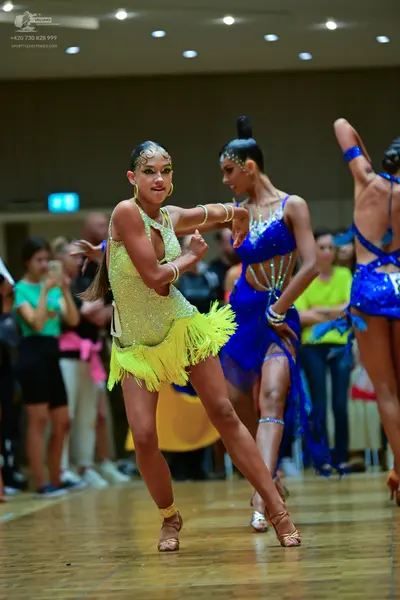 Dancesport competitor: Female dancer in foreground: lime green/yellow sequined latin dress with fringe