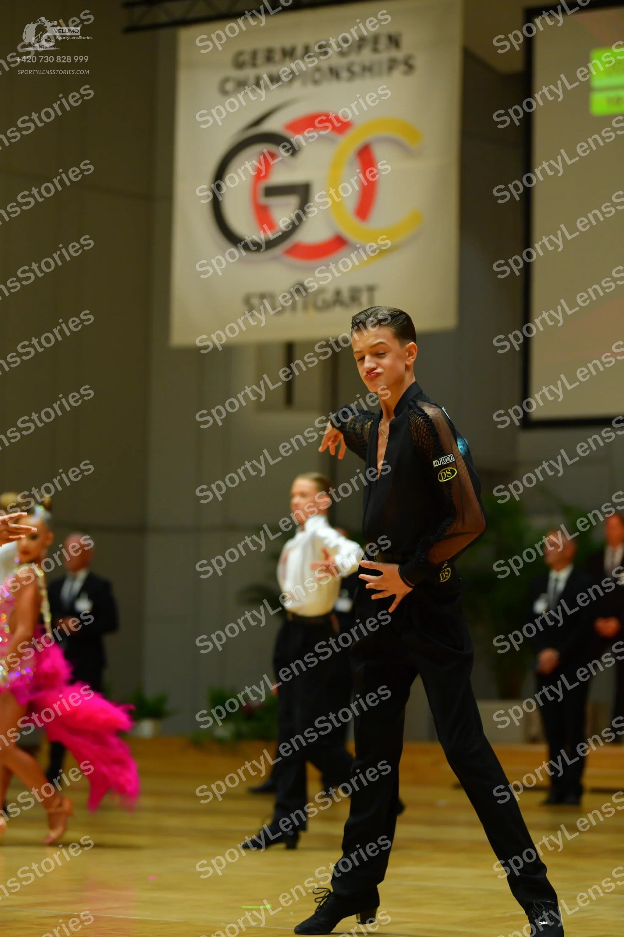 Dancesport competitor: Male dancer (foreground): black long-sleeved top with sheer sleeves and black tr