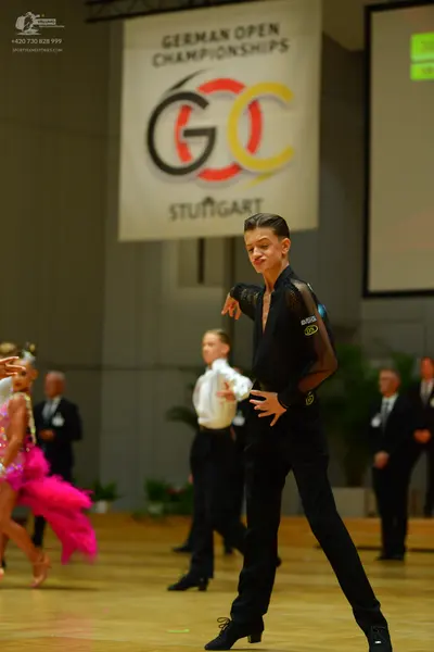 Dancesport competitor: Male dancer (foreground): black long-sleeved top with sheer sleeves and black tr