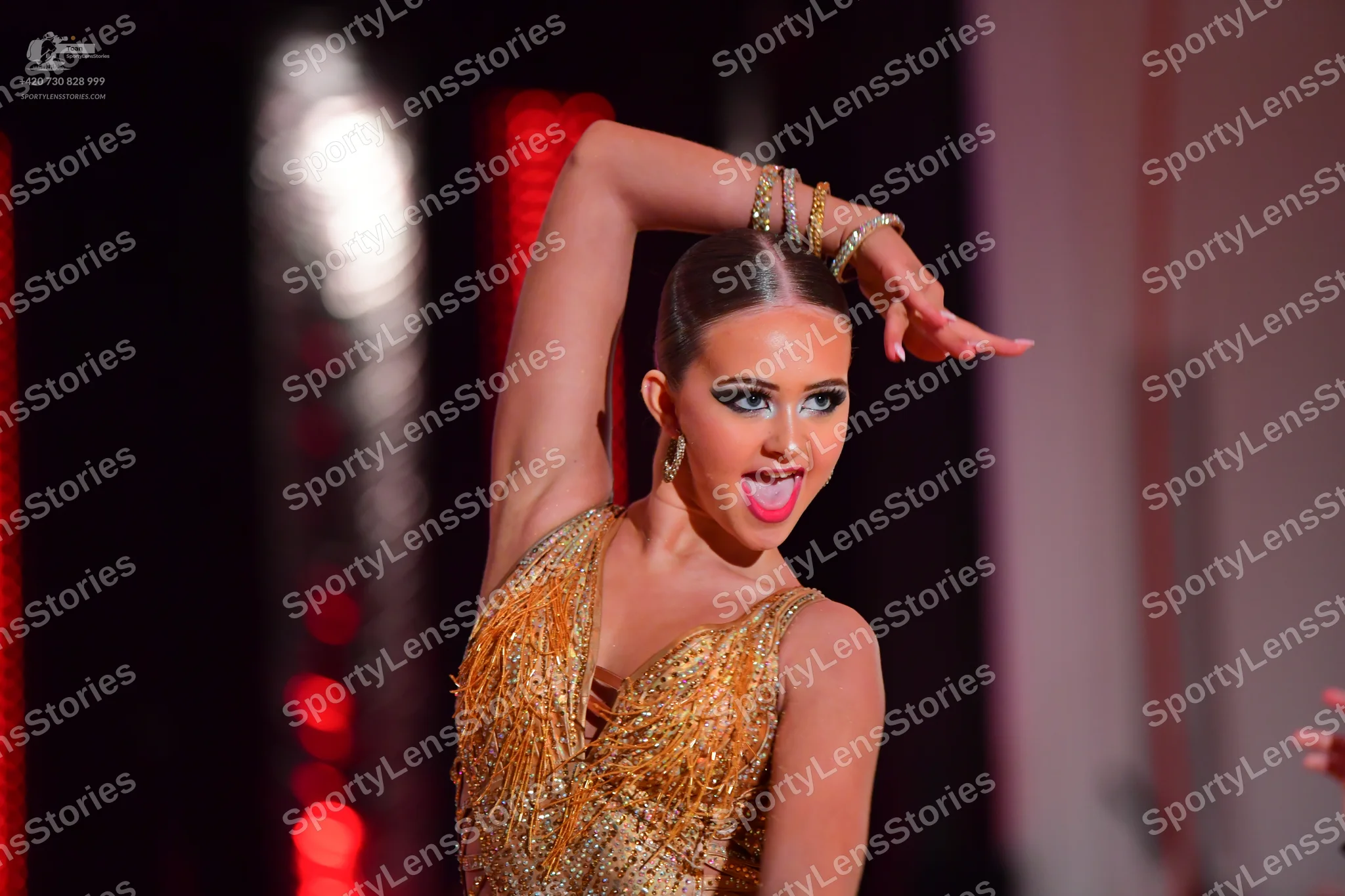 Dancesport competitor: Female dancer: gold, sequined Latin dance top with a V-neckline, wearing multipl