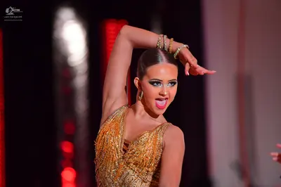 Dancesport competitor: Female dancer: gold, sequined Latin dance top with a V-neckline, wearing multipl
