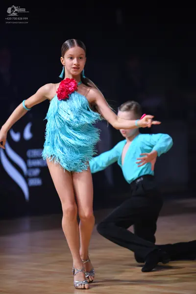 Dancesport competitor: Female dancer: light blue fringed latin dress with a large red flower embellishm