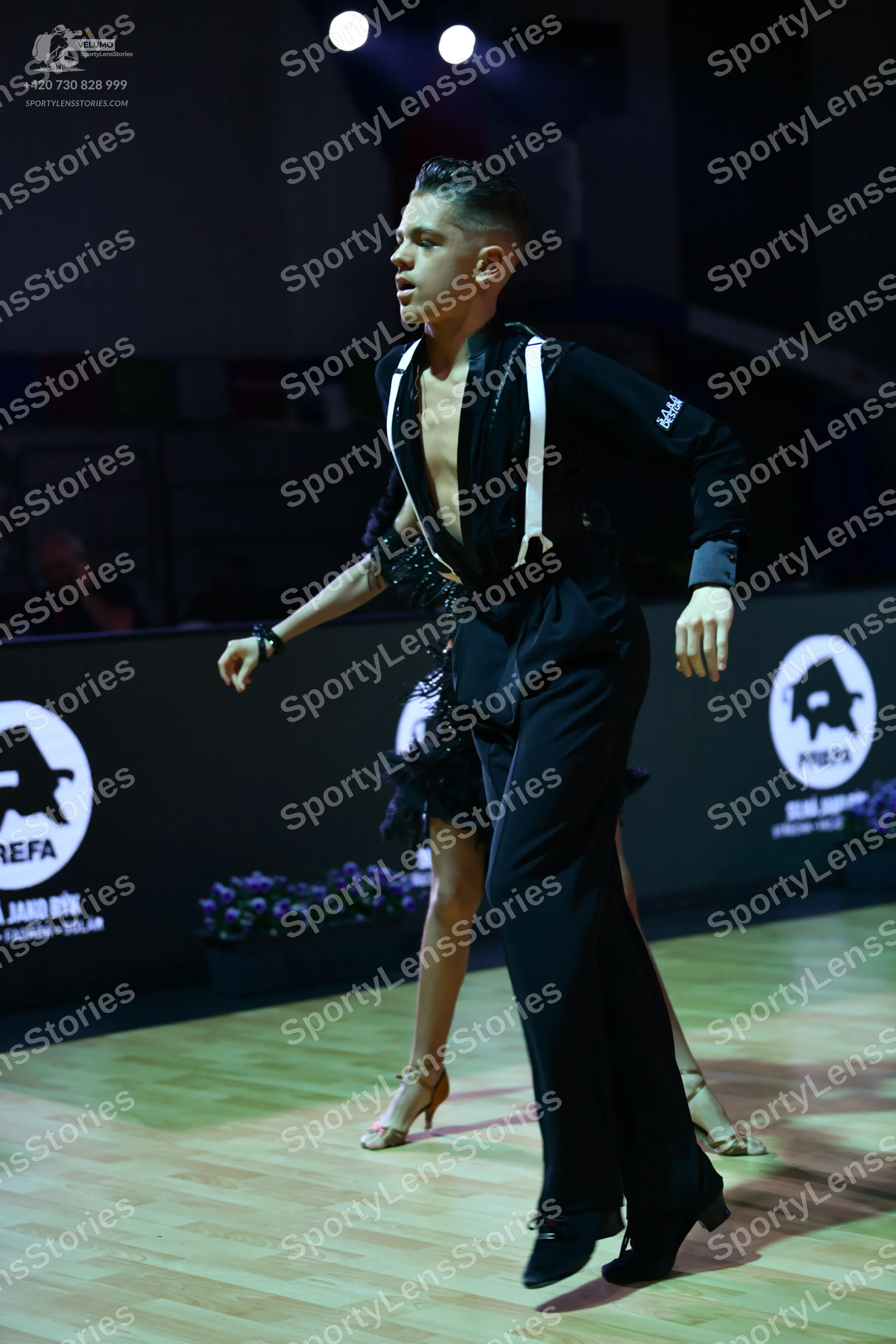 Dancesport competitor: Male dancer: black Latin dance costume with white/silver vertical trim on the to