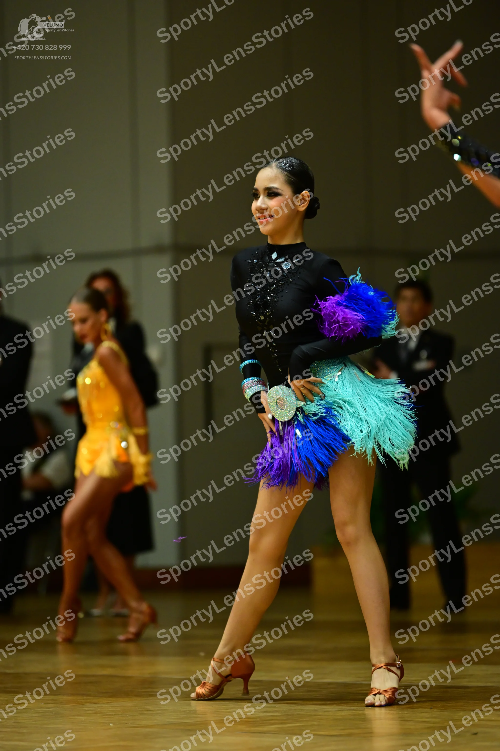 Dancesport competitor: Female dancer in foreground: black long-sleeved Latin dress with a high neckline