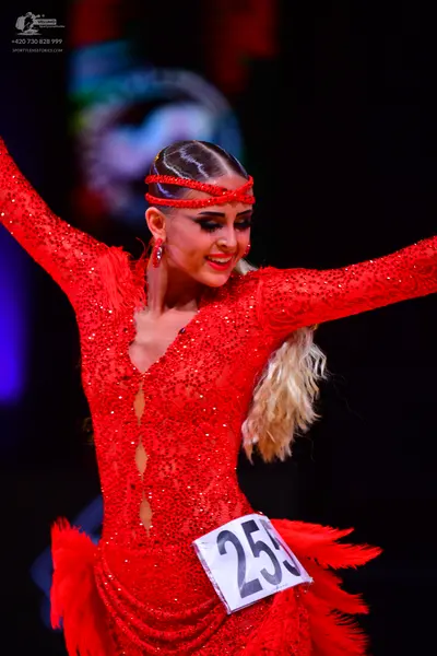 Dancesport competitor: Female dancer: red latin dress with sequins and fringe/feathers, featuring a mat