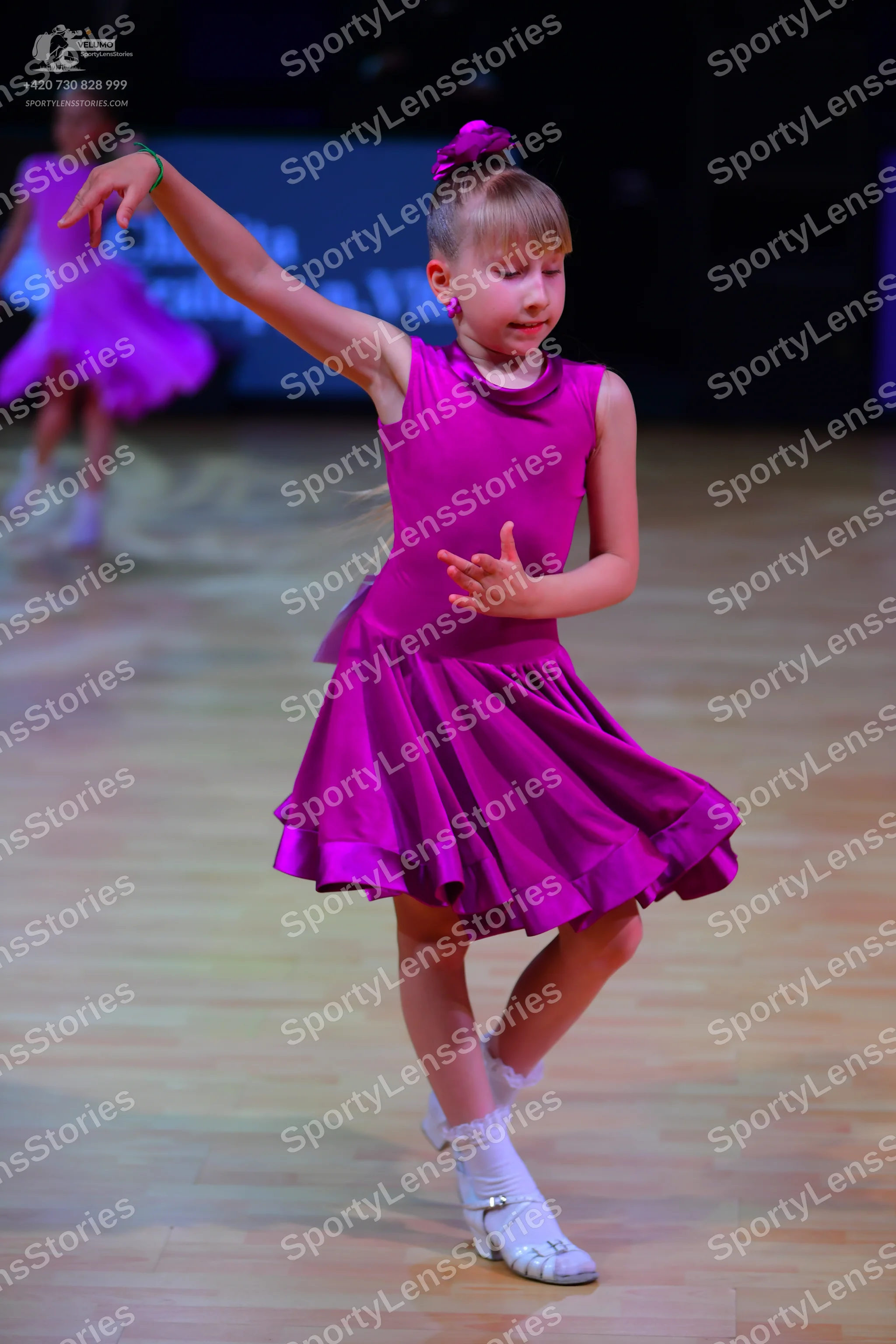 Dancesport competitor: Female dancer in foreground: magenta sleeveless dress with a flared, ruffled ski
