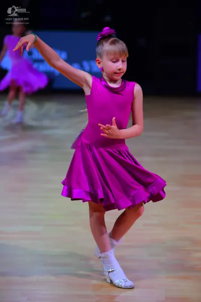 Dancesport competitor: Female dancer in foreground: magenta sleeveless dress with a flared, ruffled ski