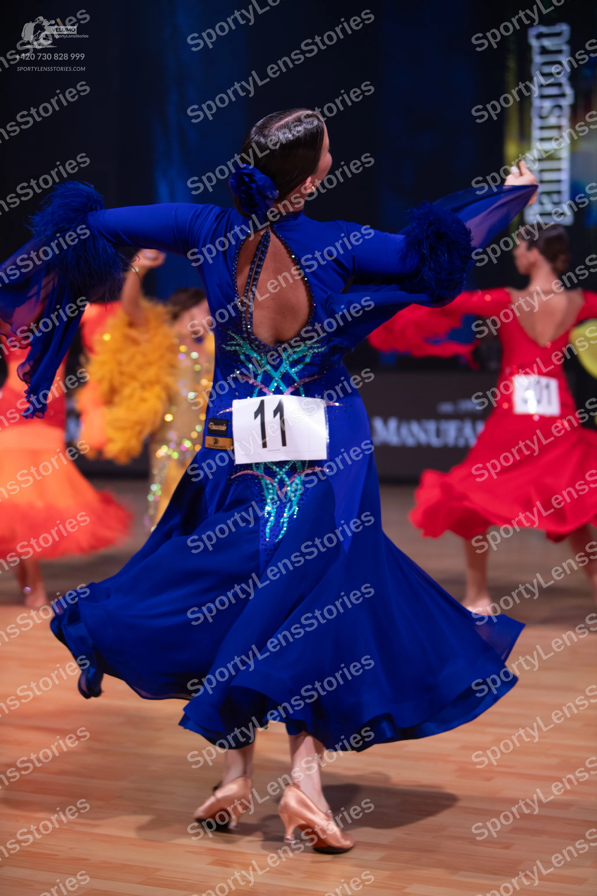 Dancesport competitor: Female dancer in foreground: blue Latin dance dress with long sleeves, a deep op