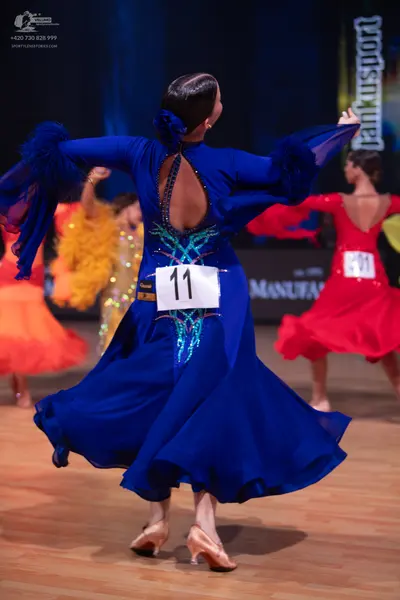 Dancesport competitor: Female dancer in foreground: blue Latin dance dress with long sleeves, a deep op