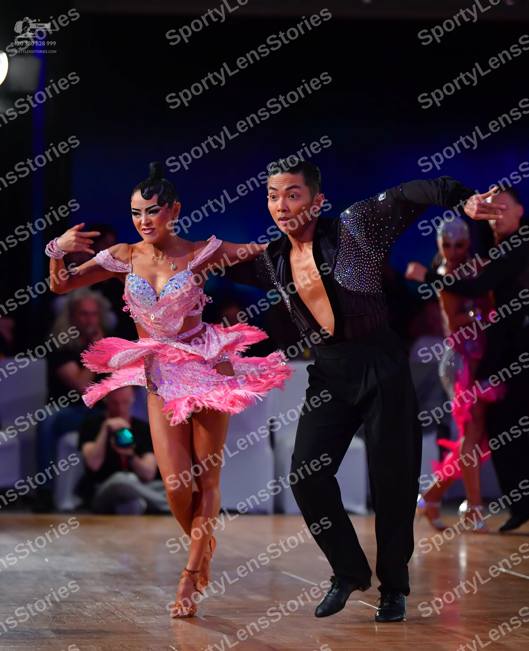 Dancesport competitor: Primary female dancer: pink latin dress with sequins, lace, and feathers, and a
