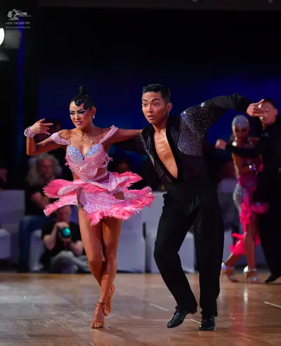 Dancesport competitor: Primary female dancer: pink latin dress with sequins, lace, and feathers, and a 