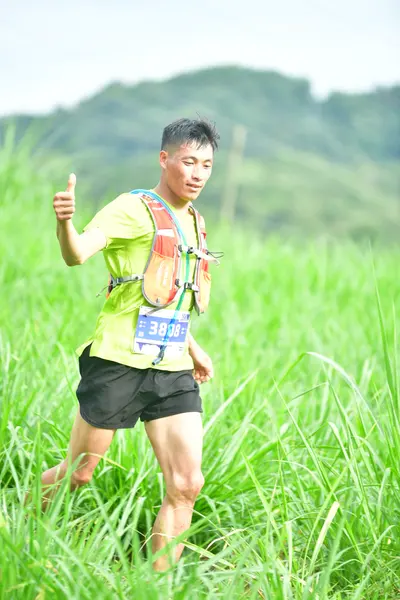 Marathon runner #3838: Runner 1: lime green shirt, black shorts, orange and white hydration vest
