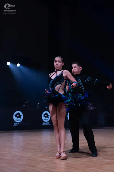 Dancesport competitor: Female dancer: black and teal latin dance costume with a ruffled, layered skirt 