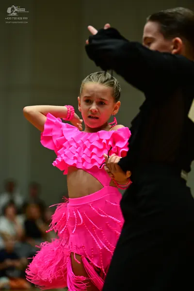 Dancesport competitor: Female dancer: bright pink Latin dance dress with ruffles and fringe, and pink b