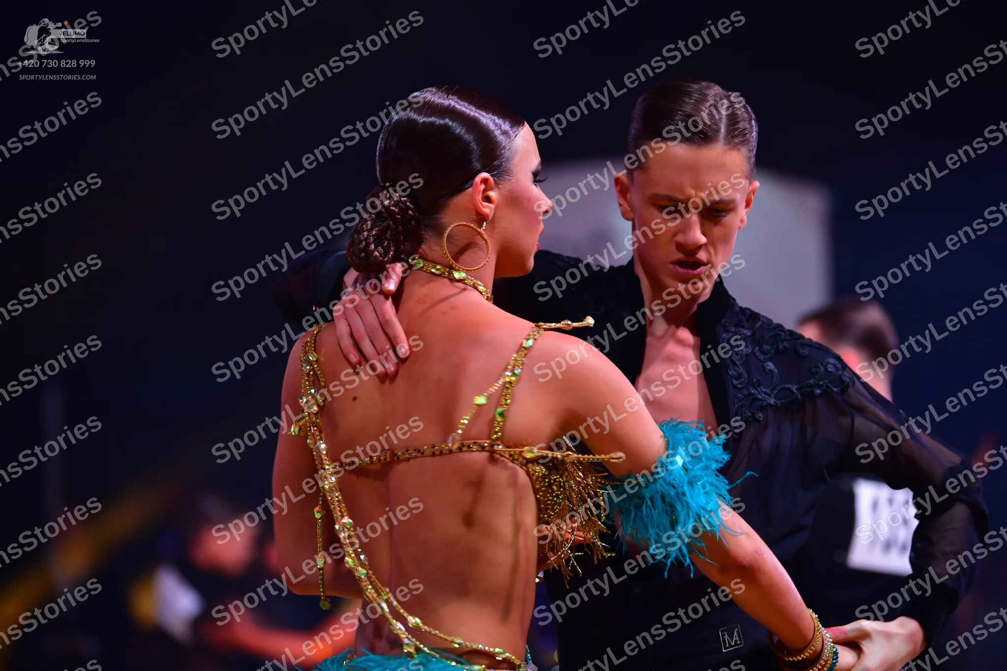 Dancesport competitor: Female dancer: backless Latin costume with gold sequined straps and turquoise/te
